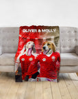 Personalized pet blanket with two dogs in red soccer jerseys, named Oliver & Molly, on a gray sofa.