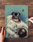 Personalized pet puzzle featuring a black pug in an astronaut suit, with hands assembling pieces.